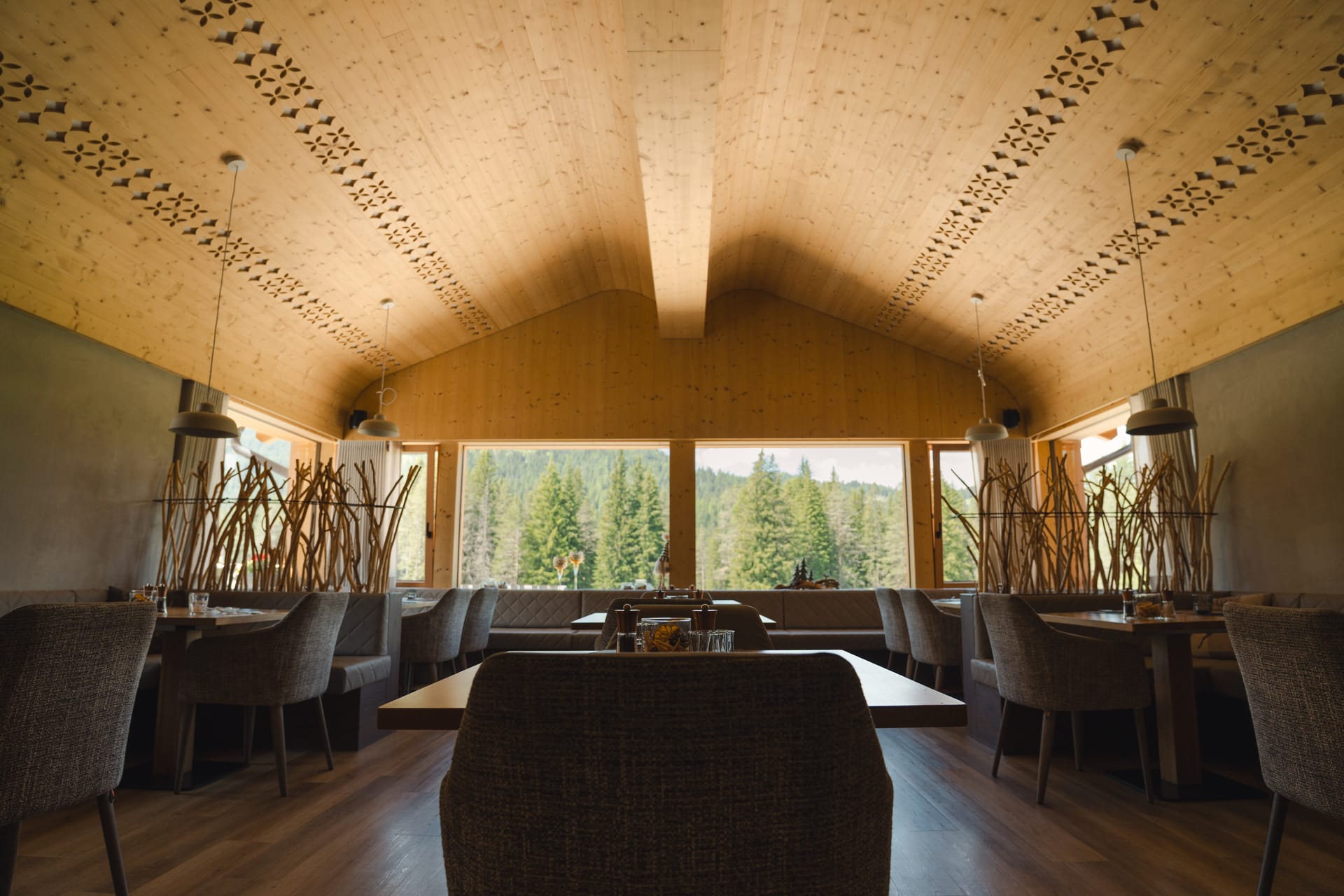 The dining room of La Raisc restaurant in San Cassiano: a carved wooden ceiling and tall windows onto the forest. Photograph by Luca Canins.