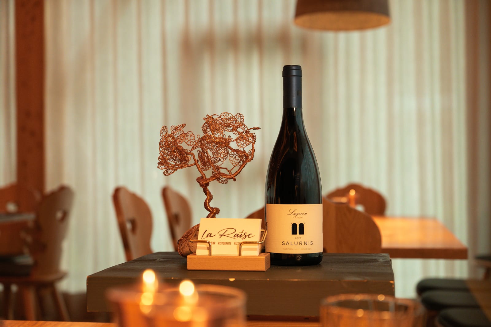 A table laid at La Raisc in San Cassiano: a bottle of wine, the restaurant’s place card and lit candles. Photograph by Luca Canins.