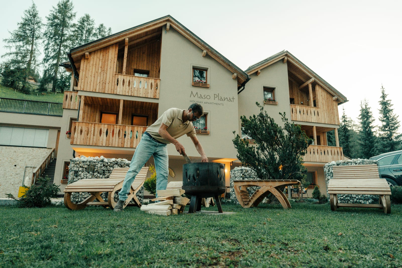 Maso Planat in San Cassiano: in front of the house, someone tends the fire bowl between wooden loungers. Photograph by Luca Canins.